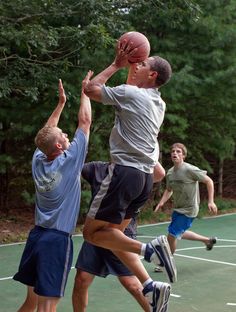 three young men playing basketball on an outdoor court with trees in the backgroud