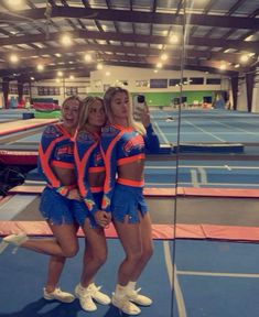 three cheerleaders taking a selfie in front of a mirror at an indoor track