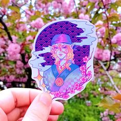 a person holding up a sticker in front of pink flowers