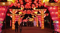 people are walking under red and yellow lanterns in the dark, with lights on them