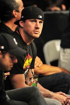 a man sitting next to another man in a black shirt and hat at a game