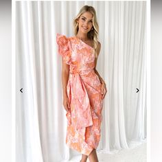 a woman standing in front of a white curtain wearing an orange and pink floral dress