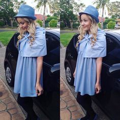 a woman standing next to a black car wearing a blue dress and hat with bow