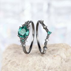 two wedding rings with green stones on top of each other, sitting on a rock