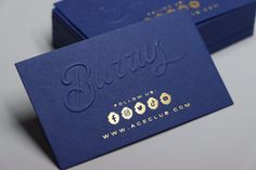 two blue business cards sitting on top of each other next to each other with gold lettering