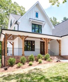 a white house with black trim and wood accents on the front porch is surrounded by trees