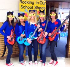 four girls in blue shirts holding guitars and wearing cat masks on their faces while standing next to each other