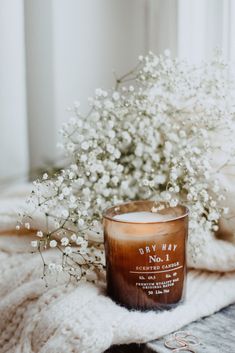 a candle sitting on top of a white blanket next to a bouquet of baby's breath