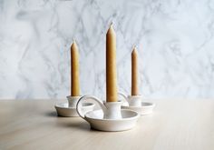 three candles sitting on top of a wooden table next to white cups and saucers