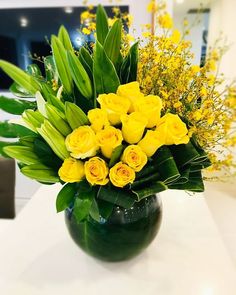 a green vase filled with yellow flowers on top of a table