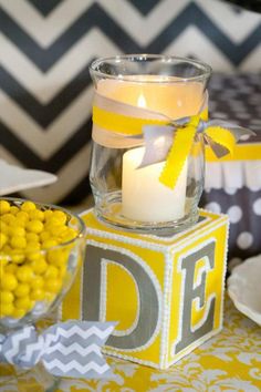 a yellow and gray table setting with a glass candle holder, bowl of candies, and chevron napkins