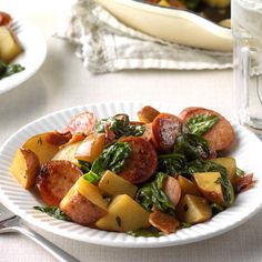 a white plate topped with potatoes and spinach next to a glass of water on a table