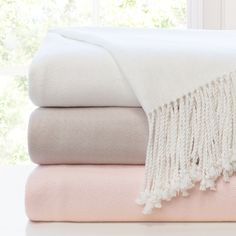 a stack of blankets with tassels on top of each other in front of a window