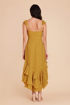 the back of a woman wearing a mustard colored dress with ruffles on it