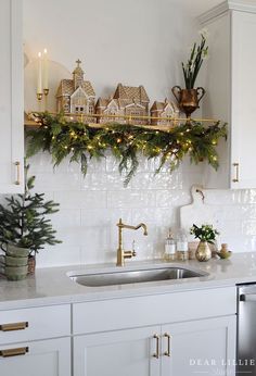 a kitchen decorated for christmas with lights and greenery on the shelf above the sink