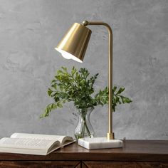 an open book on a table next to a lamp and vase with a plant in it