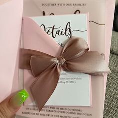 a person holding up a pink and silver wedding card with a bow on it's side