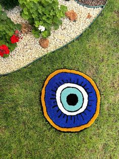 a blue and yellow rug with an eyeball on it in the grass next to some flowers