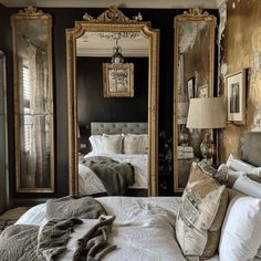 a bedroom with black walls and gold mirrors on the wall, white bedding and pillows