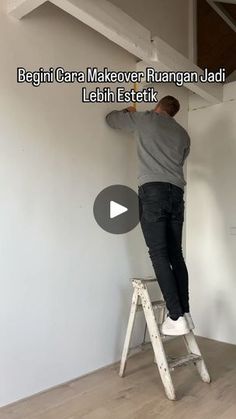 a man standing on a step ladder painting the wall with white paint in an empty room