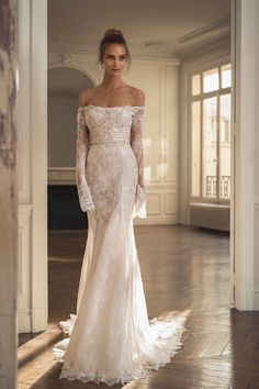 a woman in an off the shoulder wedding dress with long sleeves and lace on it