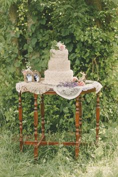 a wedding cake sitting on top of a wooden table in front of some greenery