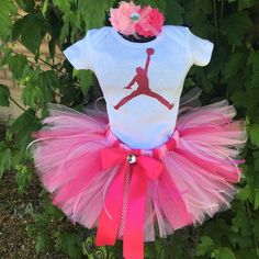 "WELCOME TO Bushels of Miracles where we add magic sprinkles to everything we make Please check my home page for shipping times and other shop details Perfection Inspired Michael Jordan Jumpman  Tutu Set in pinks and white,  includes Tutu, Bodysuit and free matching headboard headband. This listing is for a darling little pink tutu with a Bodysuit or shirt with your daughters age.  Happy to make this for your newborn, 1 year old, 2 year old, 3 year old, 4 year old, 5 year old, 6 year old, 7 year old, or 8 year old.  Can also add her name for only $6.00.  This is a hand tied tutu on commercial grade elastic for the waist.  There are ribbon streamers for that added pizzazz and a matching bow with a rhinestone center.  You will find my tutu to be of the highest quality.  Super full and fluffy Cute Pink Tutu Dress For Christmas, Fun White Tutu Dress For Birthday, Playful White Tutu Dress For Birthday, Fitted Tutu Dress For Birthday And Easter, Easter Birthday Fitted Tutu Dress, Fitted Tutu Dress For Easter Birthday, Playful Tutu Dress For Birthday And Easter, Playful Birthday Tutu Dress For Easter, Michael Jordan Jumpman