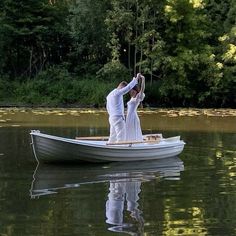 two people in a boat on the water with trees in the backgrouds