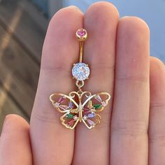 a gold butterfly belly button ring with pink, green and white stones on the side