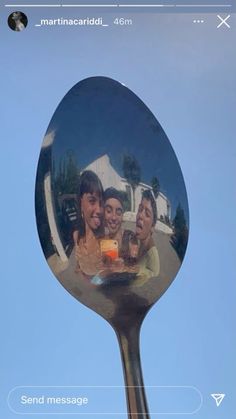 the reflection of three people in a mirror on a metal spoon with blue sky behind them