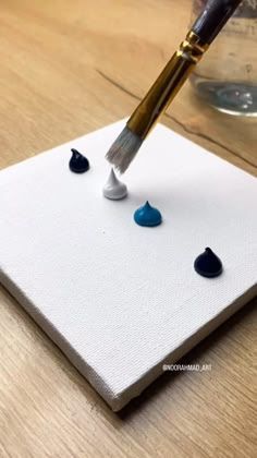 a person is using a brush to paint rocks on a piece of white paper with black and blue dots