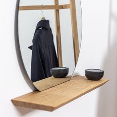 a mirror and bowl on a wooden shelf in front of a coat rack with a black robe