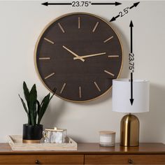 a large clock mounted to the side of a wall next to a lamp and potted plant