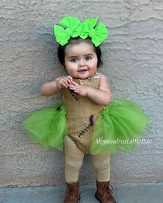 a baby girl wearing a green tutule and bow in front of a wall