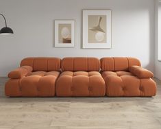 an orange couch sitting on top of a hard wood floor next to two framed pictures