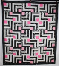 a black and white quilt with pink squares on the front is hanging from a wall