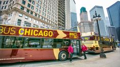 two red and yellow buses parked next to each other in front of tall buildings on a city street