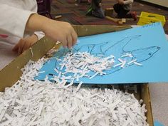 a child is cutting out paper with scissors in a box full of shredded white papers