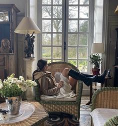 a woman laying on top of a chair in a living room next to a window