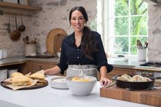 a woman standing at a kitchen counter with bowls of food in front of her,