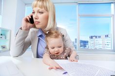 a woman sitting at a desk with a baby on her lap while talking on the phone