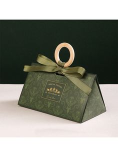 a green box with a gold ring on it's lid and ribbon around the top