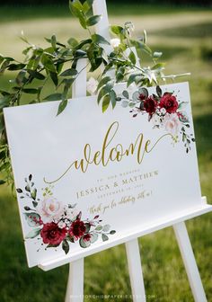 a welcome sign with red flowers and greenery on the top is sitting in front of a white easer