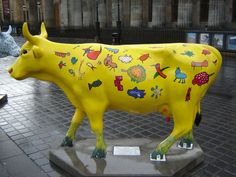 a yellow cow statue sitting on top of a sidewalk