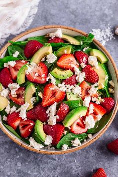 a salad with strawberries, avocado and feta cheese in a bowl