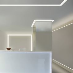 a white counter in an empty room with light coming through the ceiling and lighting up the walls