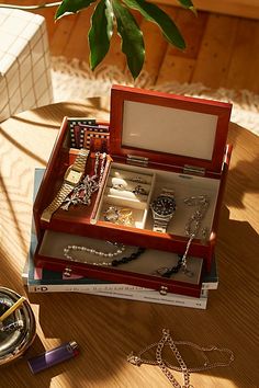 a wooden box filled with jewelry sitting on top of a table next to a potted plant