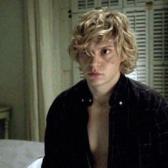 a young man with curly hair is staring at the camera while sitting on a bed