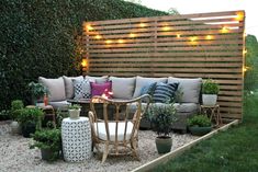 an outdoor seating area with potted plants and lights on the wall behind it, in front of a wooden privacy screen