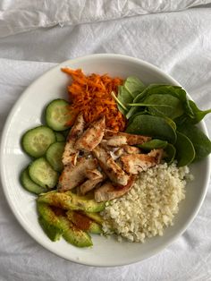 a white plate topped with rice and veggies next to sliced cucumbers